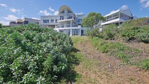 Un bâtiment moderne à plusieurs étages, doté d’un toit incurvé, entouré d’une végétation luxuriante et surplombé d’un ciel bleu clair.