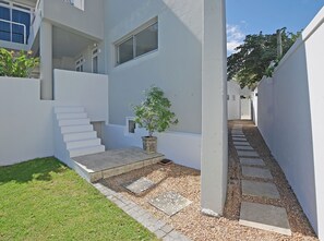 A modern building with a white exterior, a small garden area with a potted plant, and a set of stairs leading to a higher level.