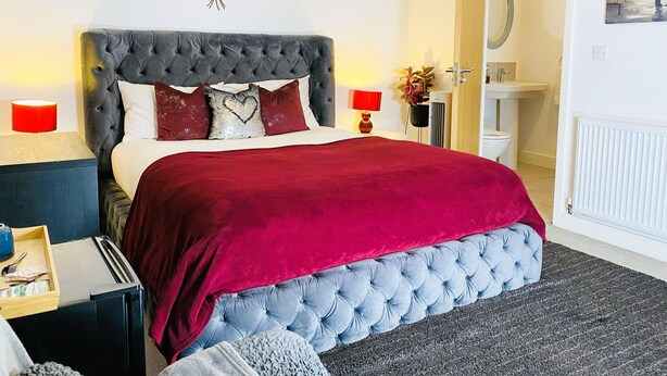 A bedroom with a tufted headboard, a red bedspread, and a wall art of leaves.
