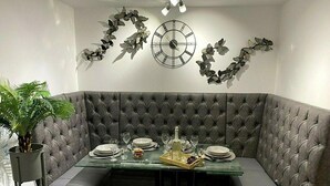 A corner dining area with a tufted grey booth, a glass table set with plates, glasses, and a bottle.