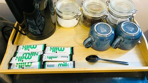 A tray with a coffee maker, jars, mugs, and milk packets.
