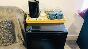 A compact black refrigerator with a wooden tray on top holding a black coffee maker, jars, and blue mugs.