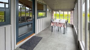 Un patio techado con una mesa, sillas, ventanas amplias y una puerta.