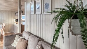 Una habitación con un revestimiento de madera, un sofá gris con cojines estampados, un helecho colgante y obras de arte enmarcadas.