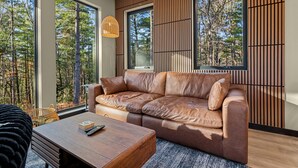 Un salon moderne avec un canapé en cuir, une table basse en bois et de grandes fenêtres donnant sur une forêt.