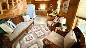 A wooden interior with a sofa, chairs, a rug, a dining table, and a kitchen area. - Eagle’s Nest Cabin • Private Forest Stay (Caddo Gap)