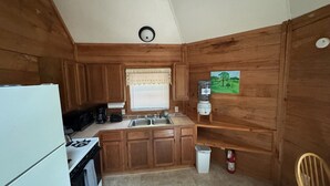 A compact kitchen with wooden cabinets, a sink, a stove, and a water dispenser. - Eagle’s Nest Cabin • Private Forest Stay (Caddo Gap)