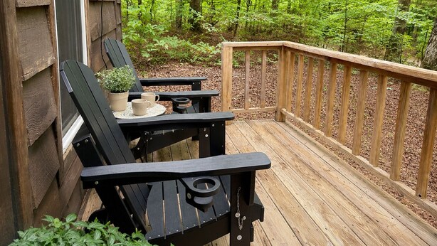 A wooden deck with two black Adirondack chairs, a small table with a potted plant, and a wooden railing. - Eagle’s Nest Cabin • Private Forest Stay (Caddo Gap)