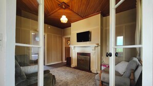 A living room with a fireplace, a television mounted above it, and a large window. - Justavacation Beachfront Bach (Riverton / Aparima)