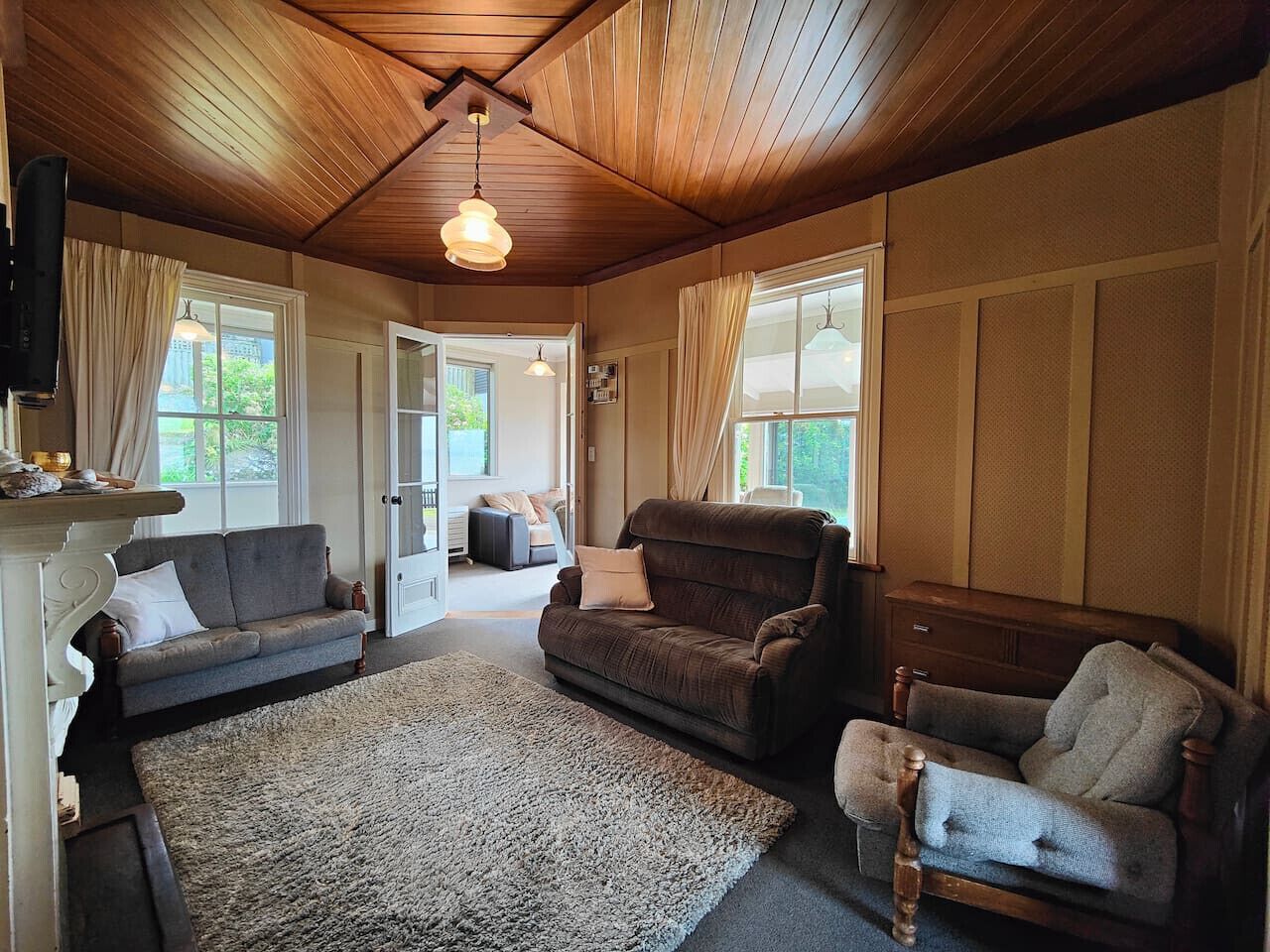 A cozy living room with wooden ceilings, a fireplace, and a large window.
