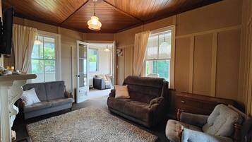 A cozy living room with wooden ceilings, a fireplace, and a large window.