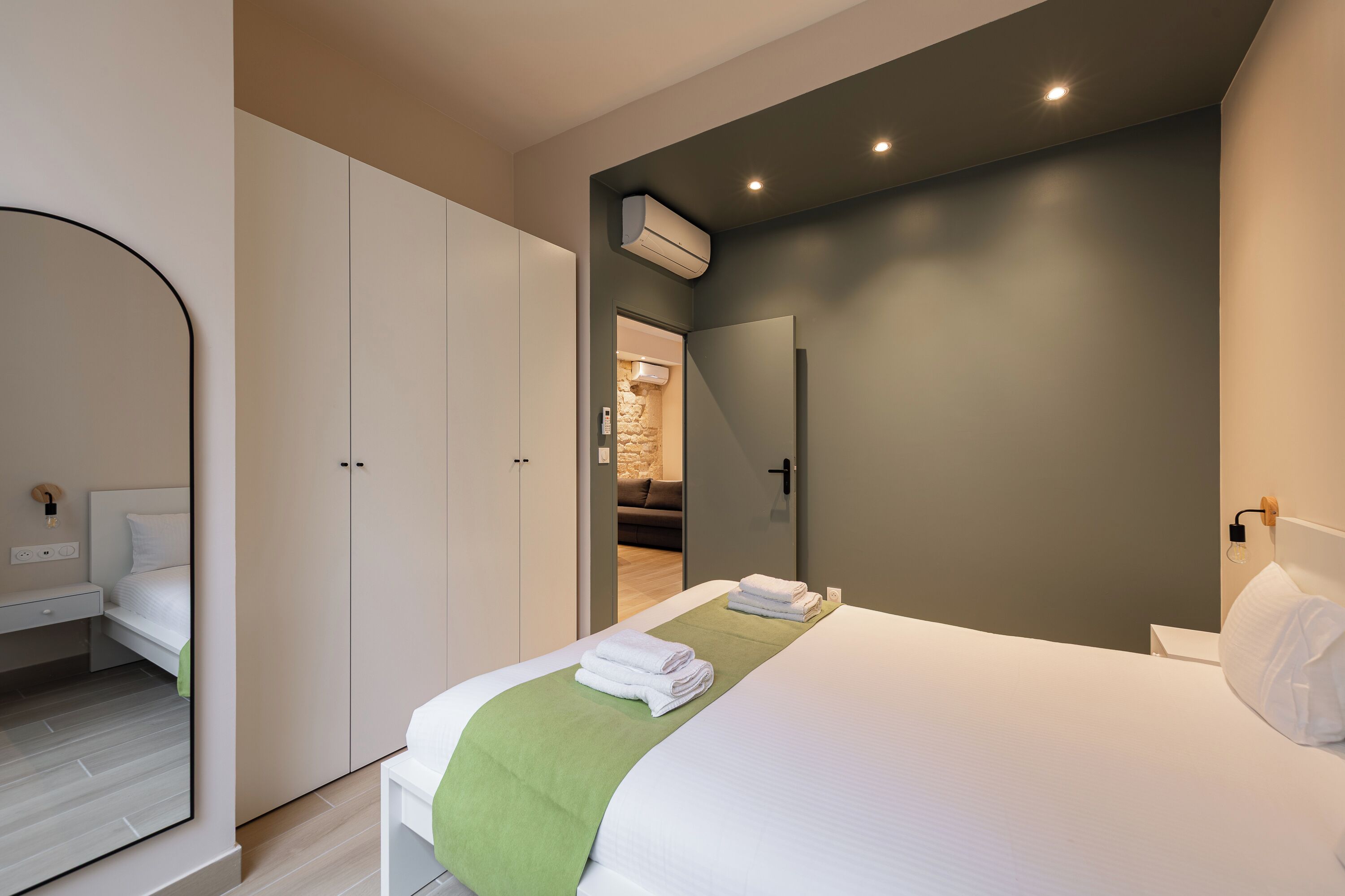 Et moderne hotelværelse med en fint opredt seng, et stort spejl og et garderobeskab.