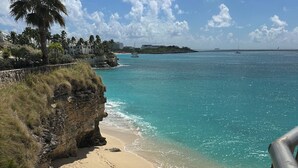 Ein Strand mit klarem türkisblauem Wasser, einem sandigen Ufer und einer Treppe, die zum Strand hinabführt.