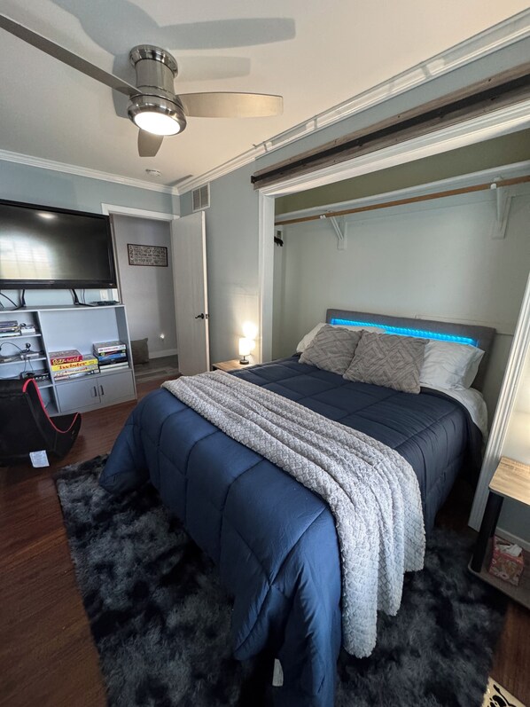 Un dormitorio con cama, televisión, escritorio y ventilador de techo.