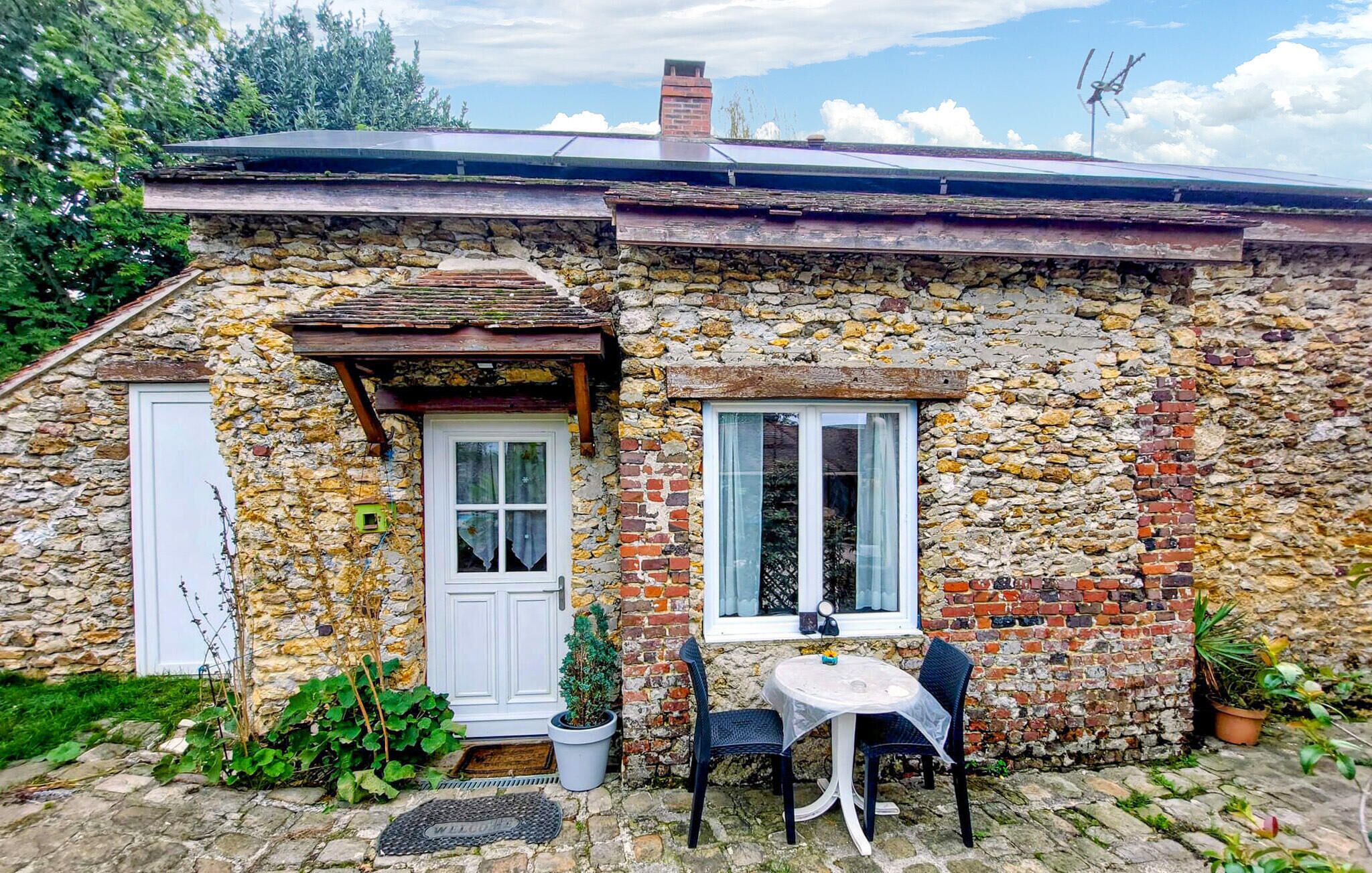 A stone house with a white door, a window, and a small table with chairs outside.