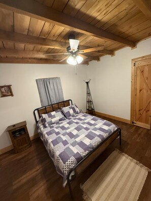 Ein Schlafzimmer mit Holzboden, einem Bett mit einem gemusterten Bettbezug, einer Stehlampe und einer Holztür.