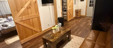A rustic interior with wooden floors, a brown leather sofa, a wooden coffee table, and a sliding barn door.