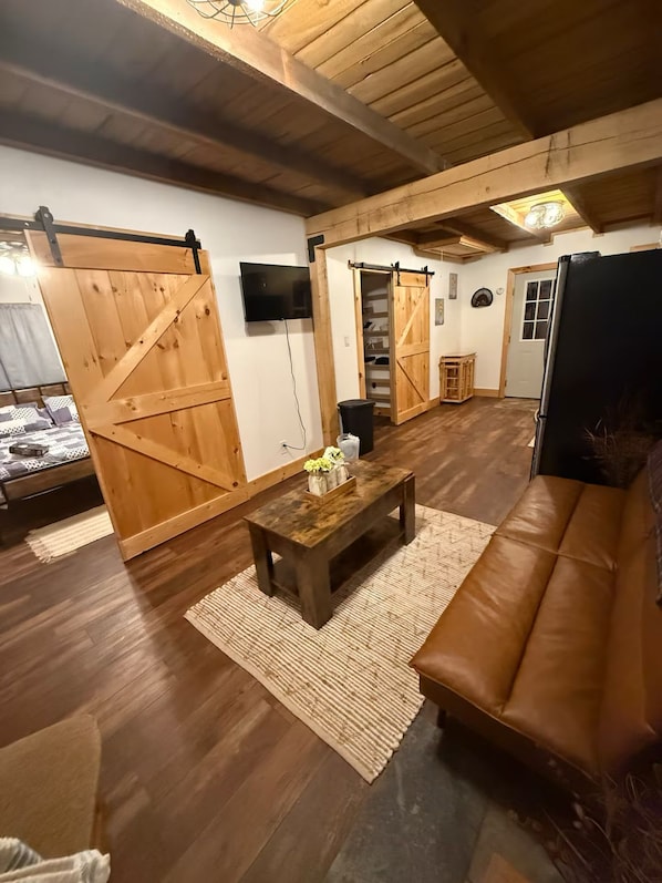 Ein rustikales Interieur mit Holzböden, einem braunen Ledersofa, einem Holztisch und einer Schiebetür im Bauernhausstil.