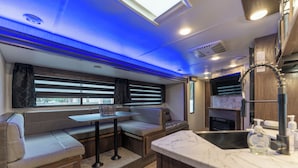 Un intérieur de camping-car compact comprenant un coin cuisine, un espace salon et une fenêtre équipée de stores.