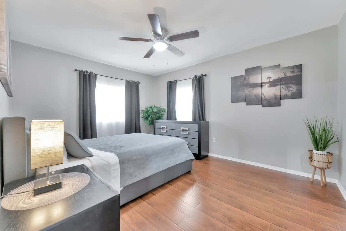 A modern bedroom with a bed, bedside table, lamp, ceiling fan, and artwork on the wall.