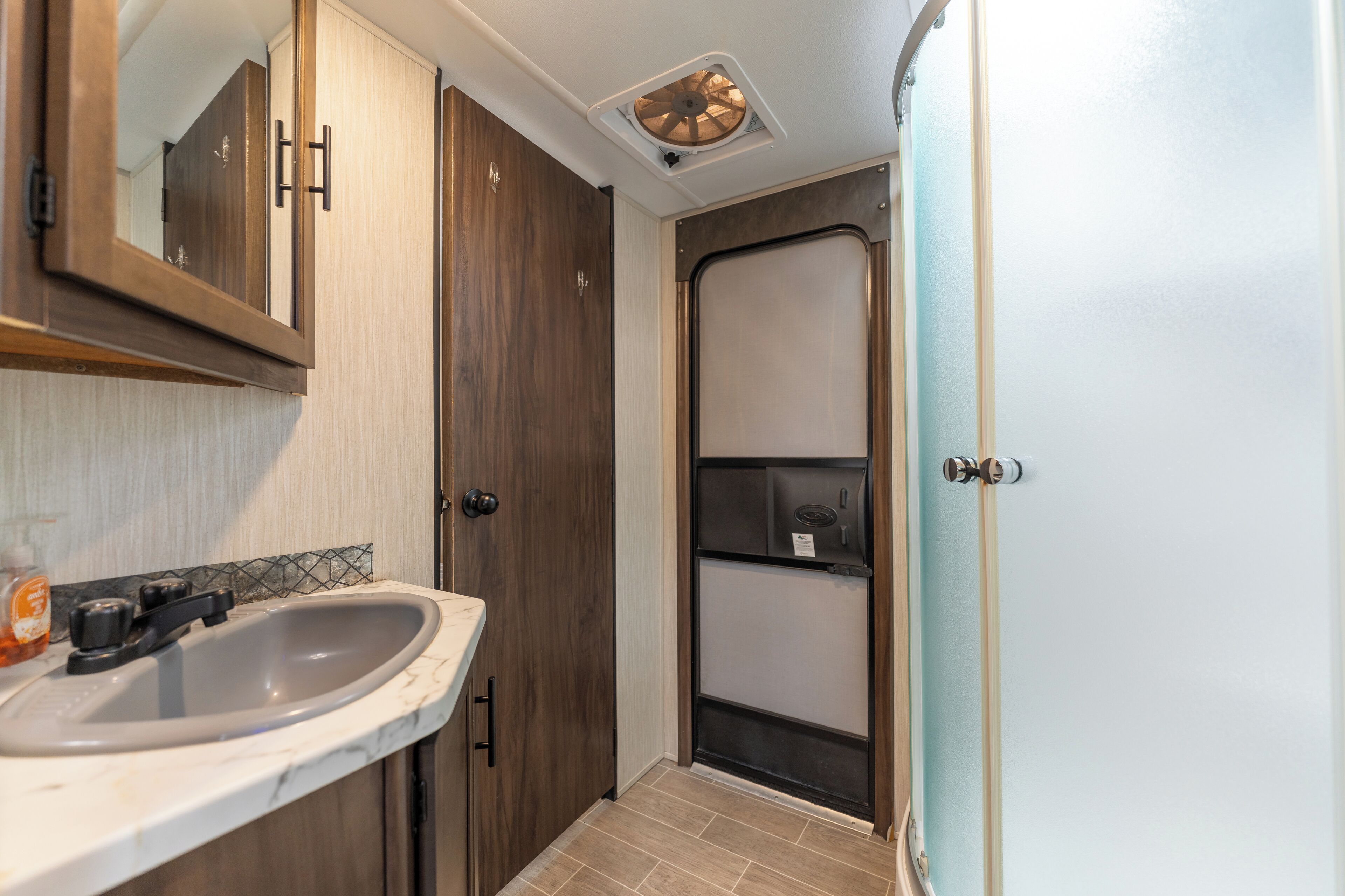 A compact bathroom with a sink, mirror, and a shower enclosure.