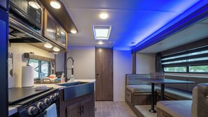 Une cuisine compacte équipée d’une cuisinière, d’un évier et d’une fenêtre donnant sur un paysage verdoyant.