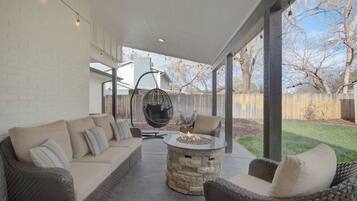 Un patio al aire libre con un hogar de piedra, muebles de mimbre y una silla colgante.