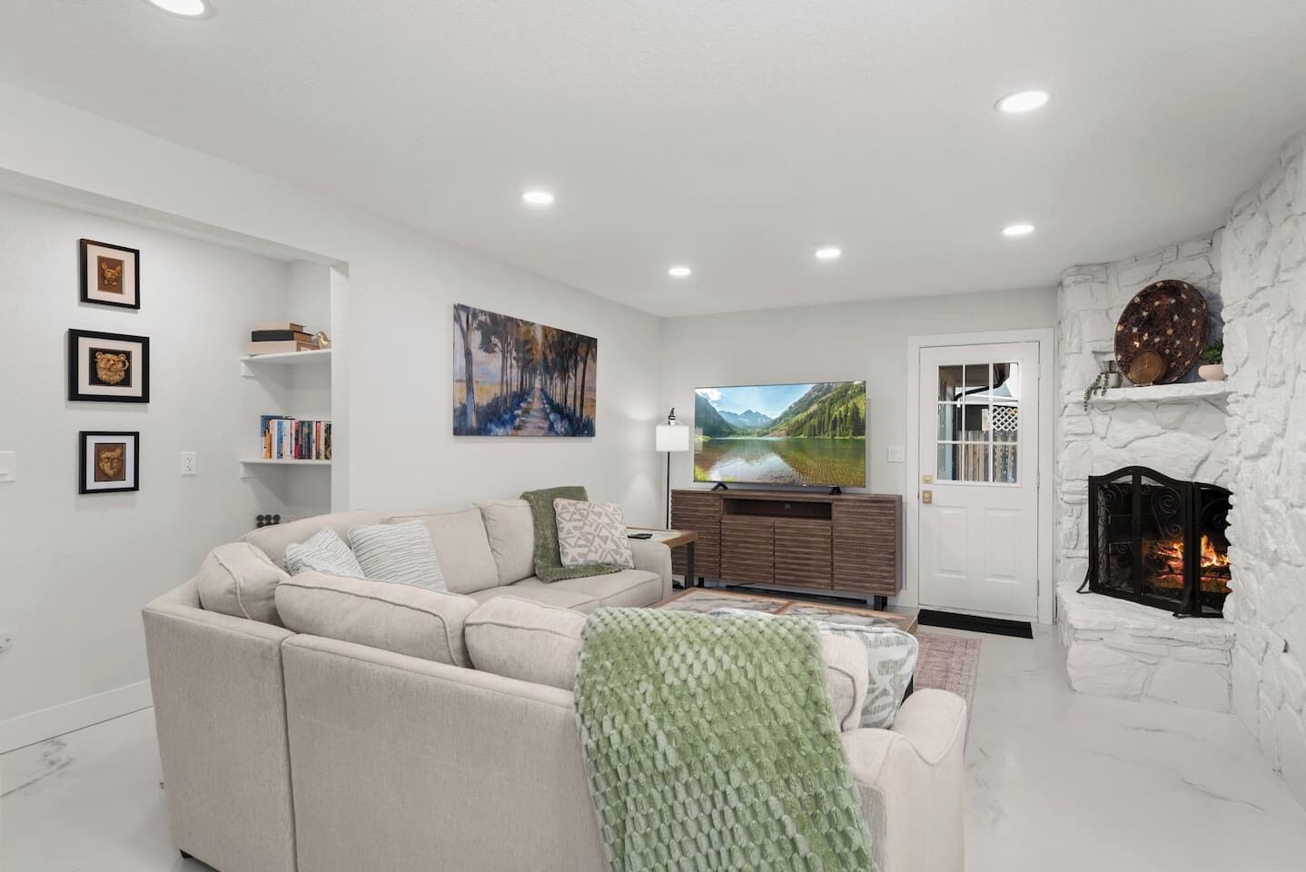 A living room with a sectional sofa, a fireplace, a TV, and artwork on the walls.