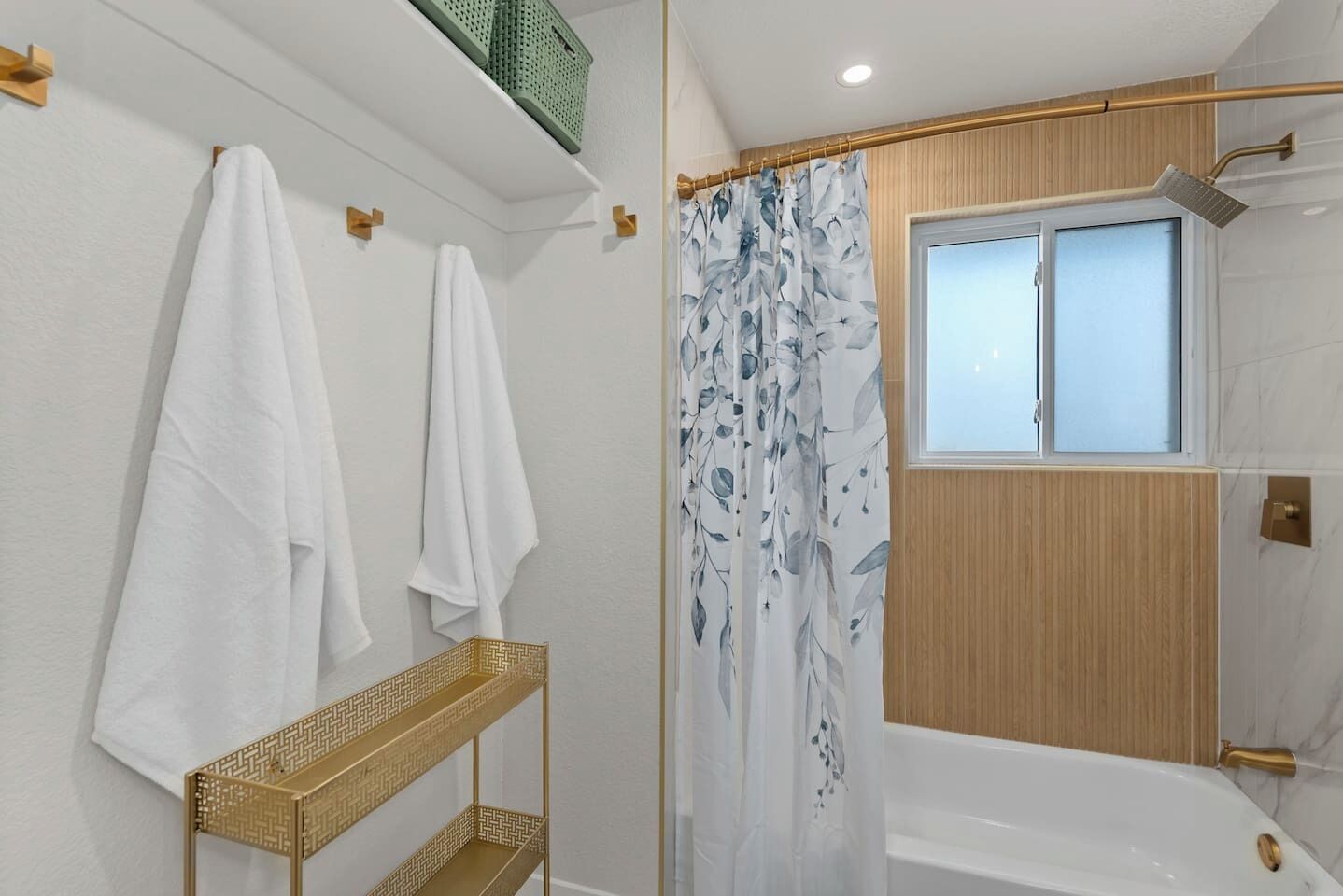 A bathroom with a bathtub, shower, and a window. There are towels hanging on the wall and a shelf with a woven basket.