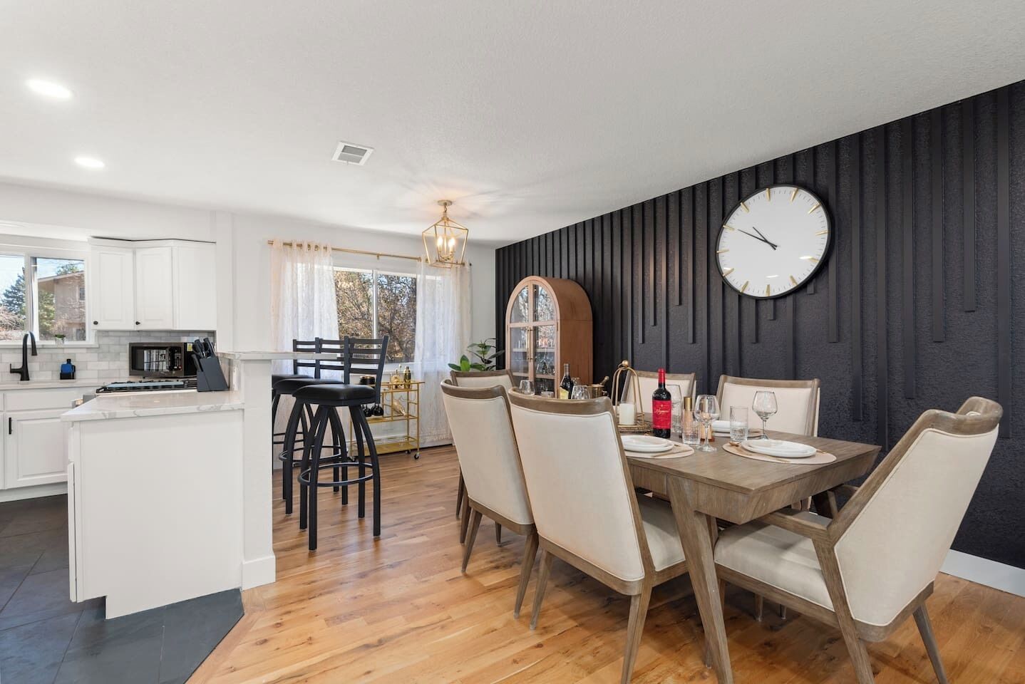 Una cocina moderna con armarios blancos, un comedor con mesa y sillas de madera, y un reloj de pared grande.