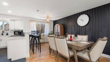 Una cocina moderna con armarios blancos, un comedor con mesa y sillas de madera, y un reloj de pared grande.