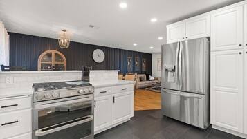 Una cocina moderna con armarios blancos, un refrigerador de acero inoxidable, un horno empotrado y una estufa a gas.