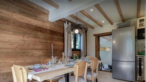 A dining area with a wooden wall, a chandelier, and a modern kitchen with a stainless steel refrigerator.