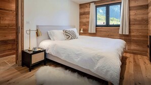 A bedroom with a wooden wall panel, a bed with white bedding, a nightstand with a lamp, and a window with curtains.