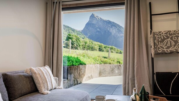 A cozy room with a sofa, a table with mugs and a tray, and a view of a mountain through a window.
