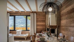 A dining area with a wooden table set for four, a large window with a view of the outdoors, and a hanging light fixture.