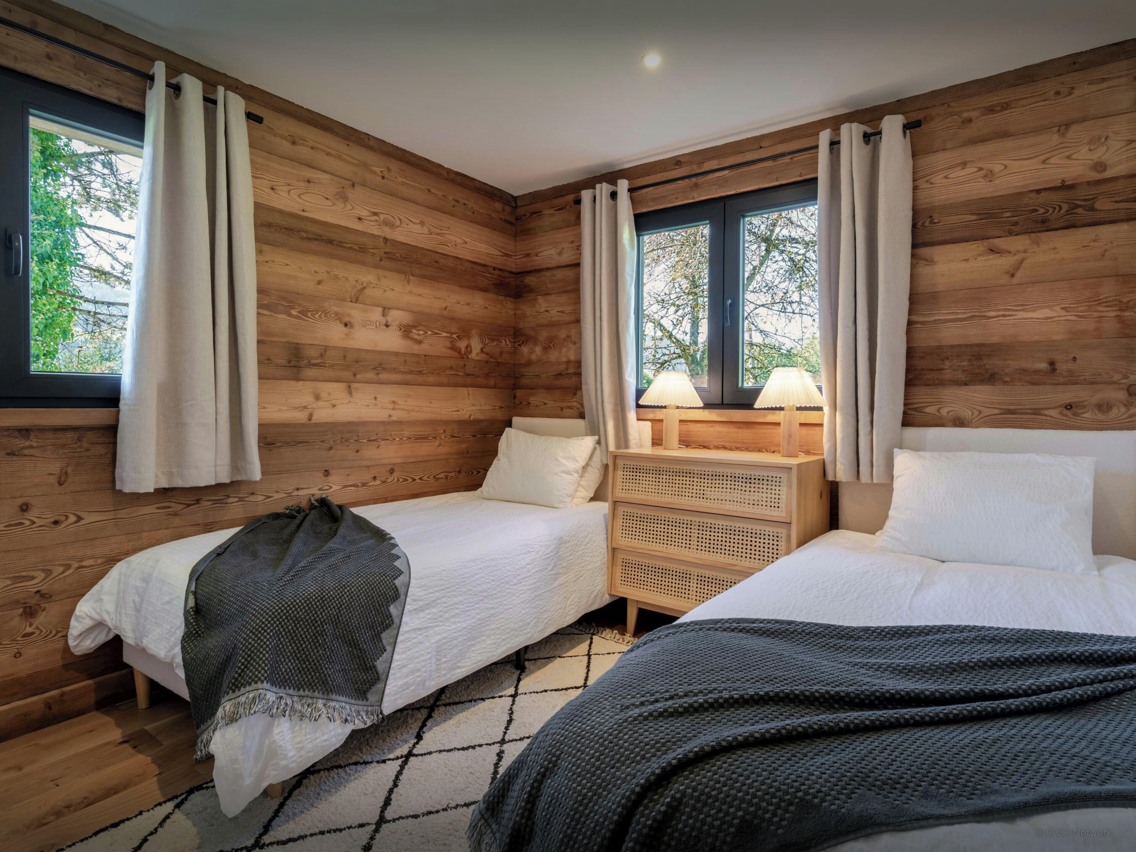 A wooden-paneled room with two beds, a nightstand, and a window with curtains.