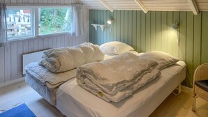 Un dormitorio con dos camas, una ventana con cortinas, una lámpara de pared y una silla de mimbre.