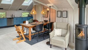 Una cocina moderna con armarios azules, un comedor con mesa y sillas de madera, un ventanal grande y un estufa de leña.