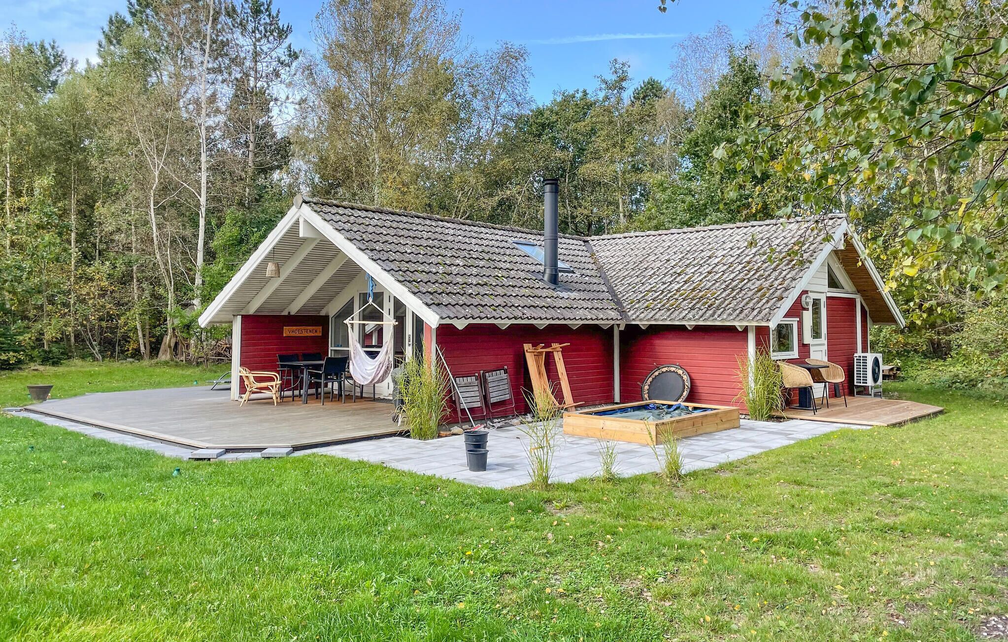 A red wooden house with a tiled roof, a deck, and a hot tub.