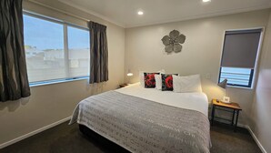 A hotel room with a large bed, two bedside tables, a nightstand, a wall clock, a decorative wall piece, and a window with curtains. - ASURE Albert Park Motor Lodge (Te Awamutu)
