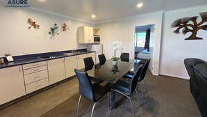A modern kitchen with white cabinets, a black countertop, and a dining area with a glass table and black chairs. - ASURE Albert Park Motor Lodge (Te Awamutu)