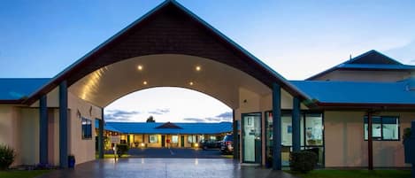 A modern hotel entrance with a covered walkway, a reception desk, and a parking area.