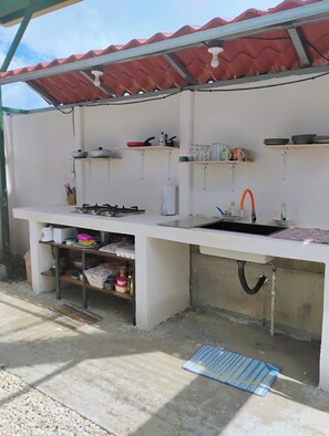 An outdoor kitchen with a gas stove, sink, and various kitchen utensils.