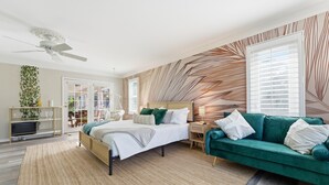 A modern bedroom with a bed, a green sofa, a ceiling fan, and a large window with blinds. - IMG Academy | Heated Pool, Game Room, Sleeps 10 (Bradenton)