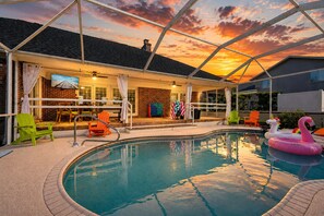 Una piscina exterior techada con vistas al atardecer, un edificio de ladrillo y juguetes inflables para la piscina.