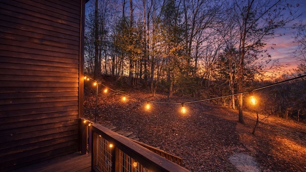 Um deck de madeira com luzes de corda, cercado por árvores e uma cabana de madeira.