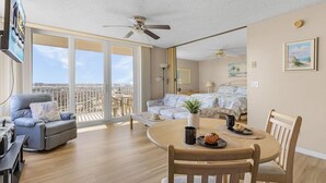A spacious living area with a balcony, a dining table with chairs, and a sofa. - Estero Beach and Tennis 1202 (Fort Myers Beach)