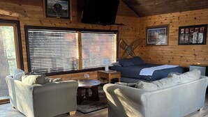 A cozy cabin interior with a wooden ceiling, two sofas, a coffee table, and a TV mounted on the wall. - Secluded Treehouse w/ River & Trail Access (Deerbrook)