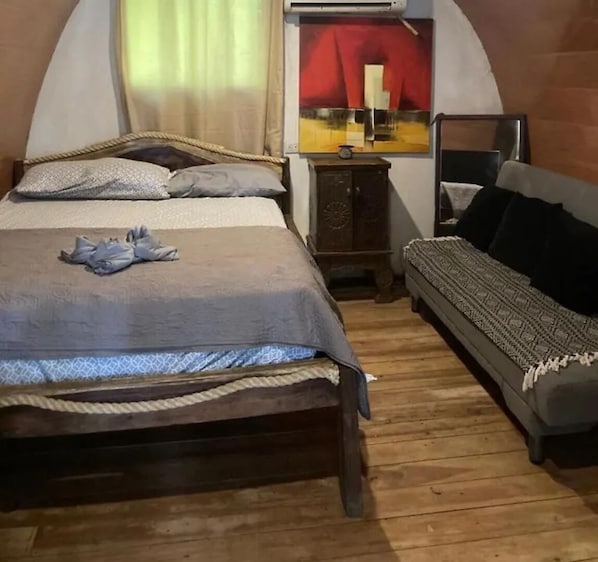 Una habitación con cama, sofá, suelo de madera y aire acondicionado de pared.